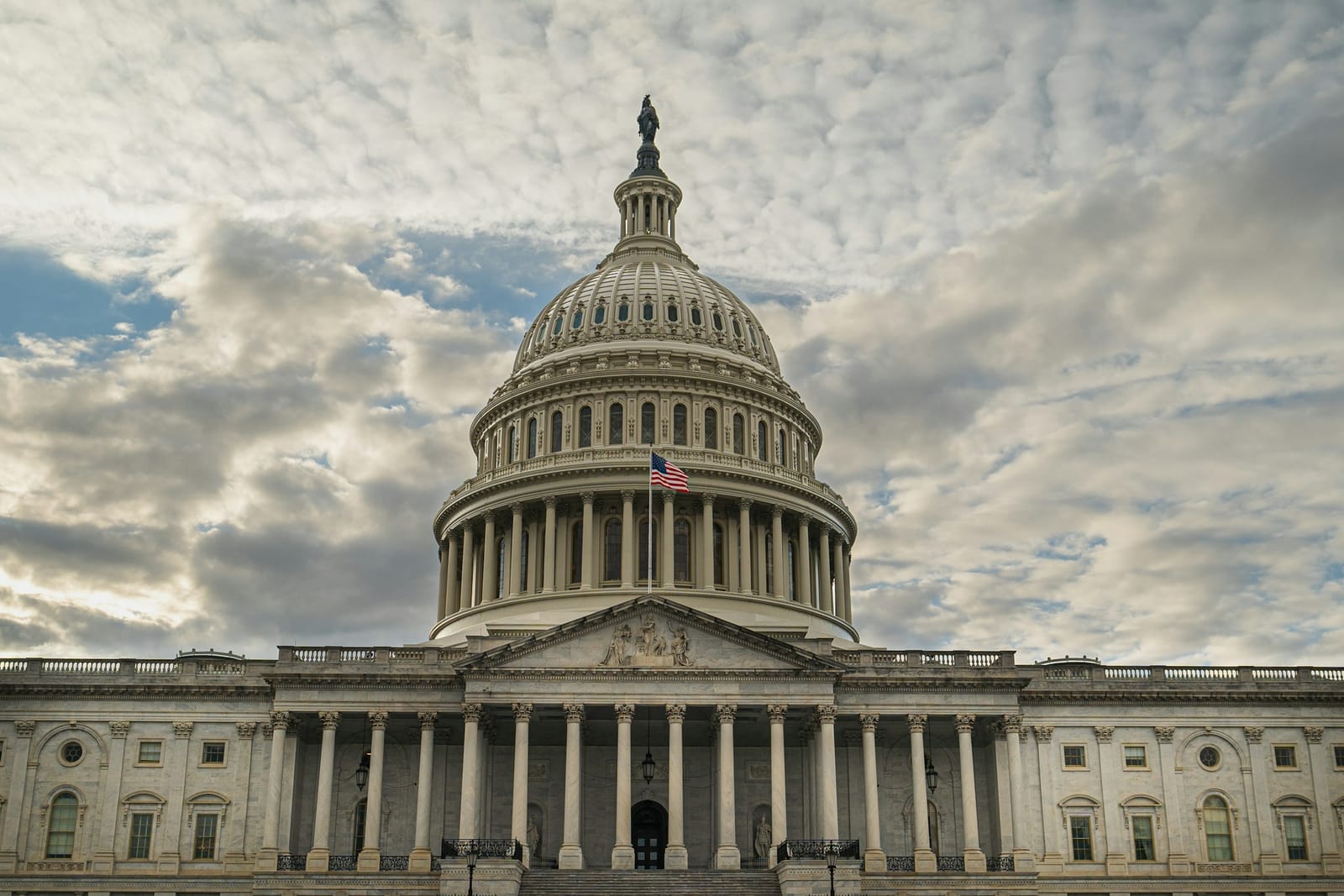 The dome of the United States Capitol under a broken, cloudy sky.