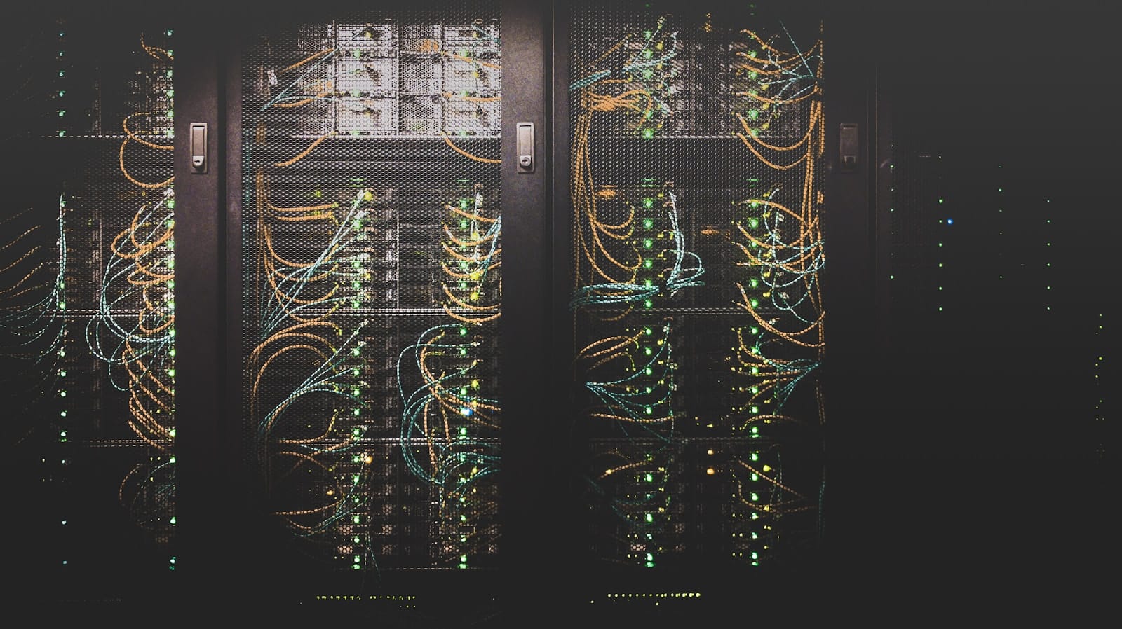 Server racks in a dark data centre with looping orange and green network cables and status lights.