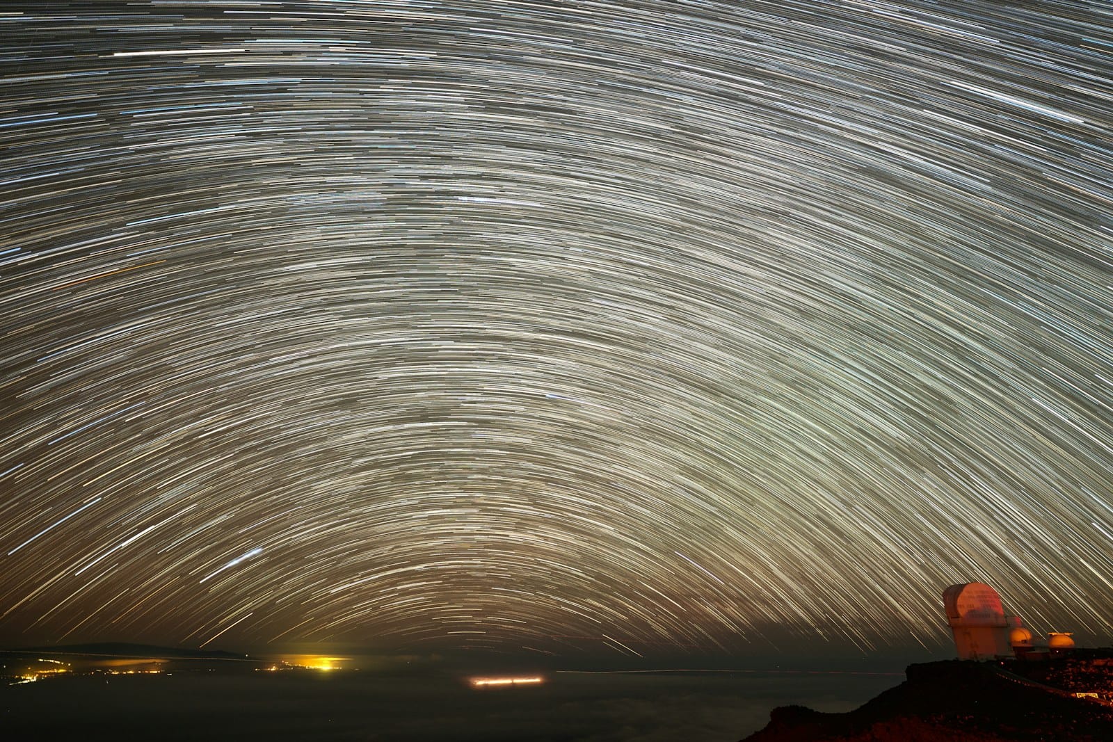 Star trails circling above a mountain-top observatory at night.