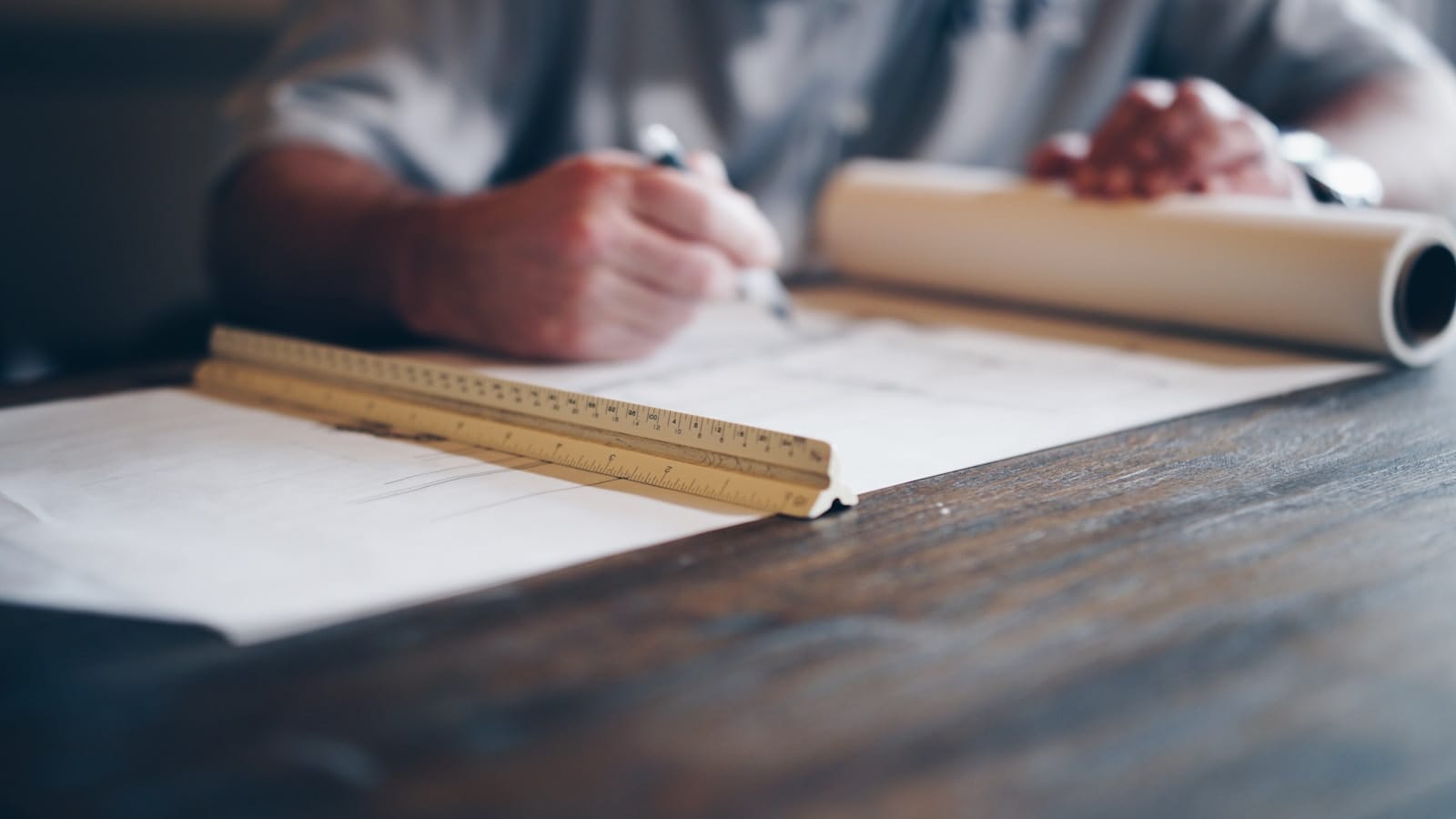 An architect drafting by hand over rolled plans.
