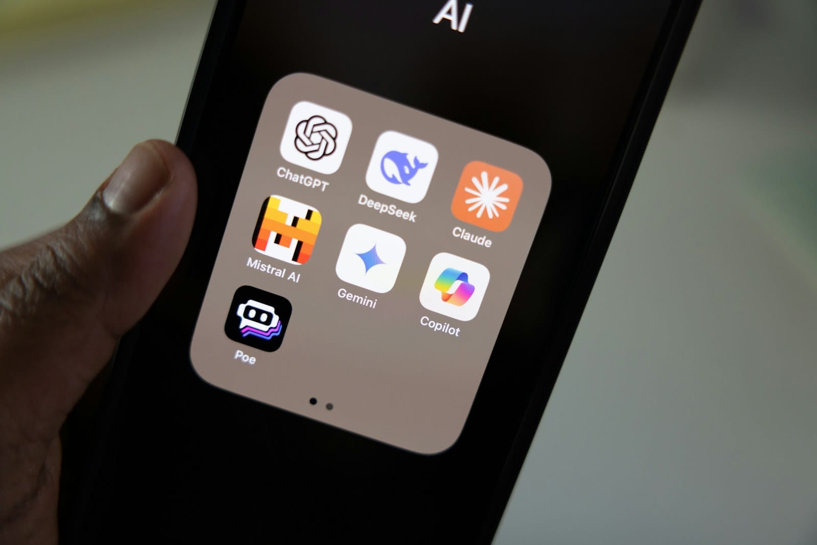 A phone showing an AI app folder with ChatGPT, Claude, Gemini, DeepSeek and Copilot.
