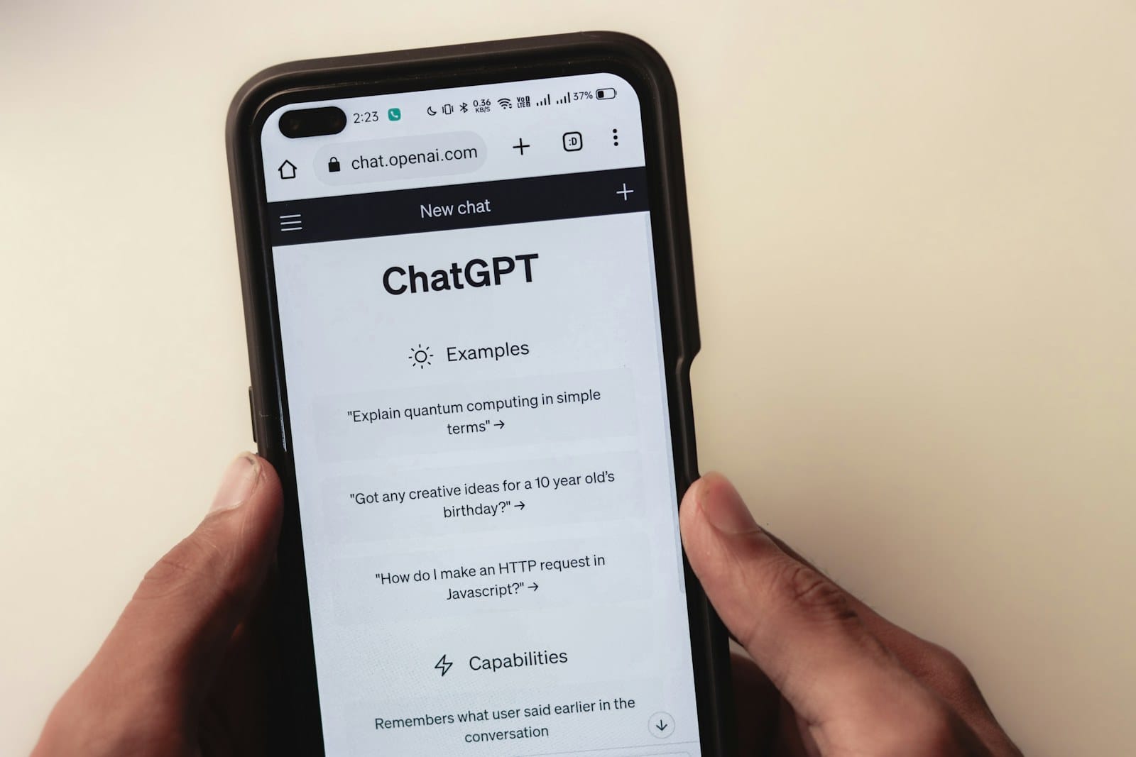 The OpenAI Introducing ChatGPT page open on a phone over an AI textbook.