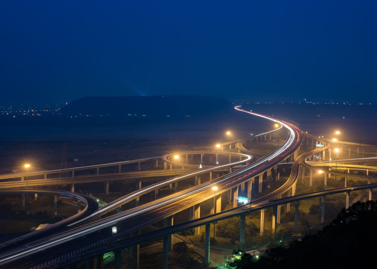 An aerial night view of a glowing motorway interchange, every route now forced through the same junction.