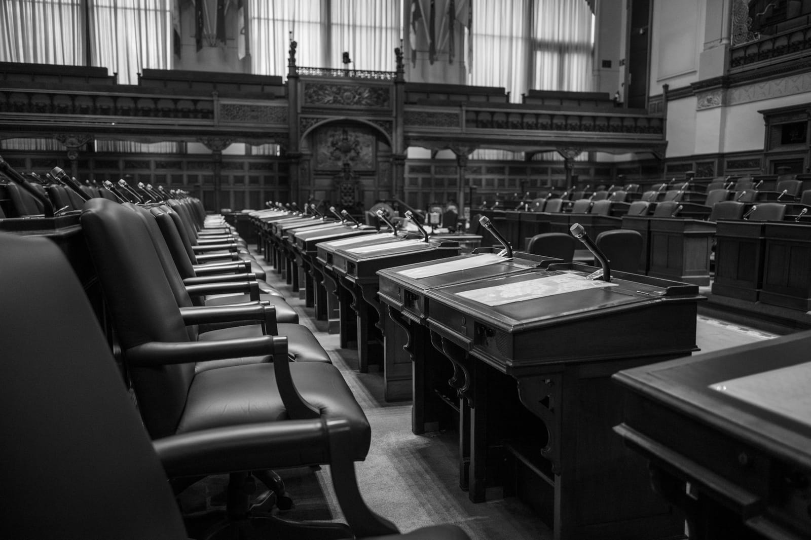 An empty legislative chamber in black and white, rows of desks and microphones waiting between sittings