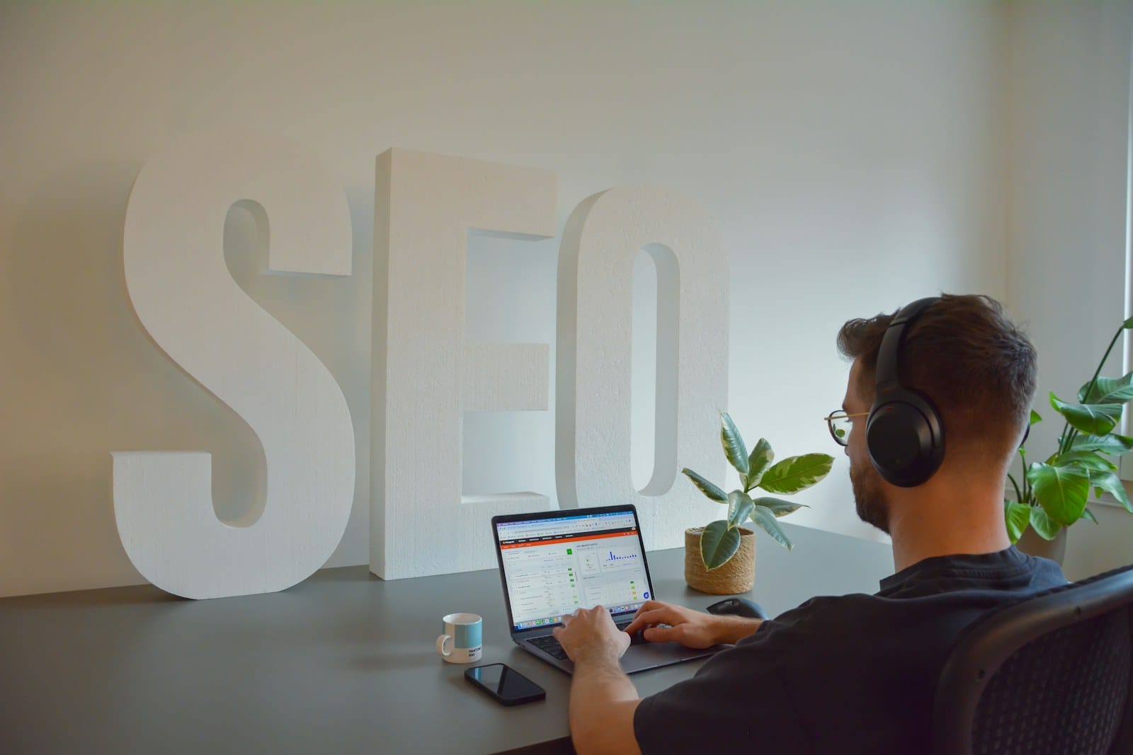 A marketer working at a laptop beside large SEO lettering.