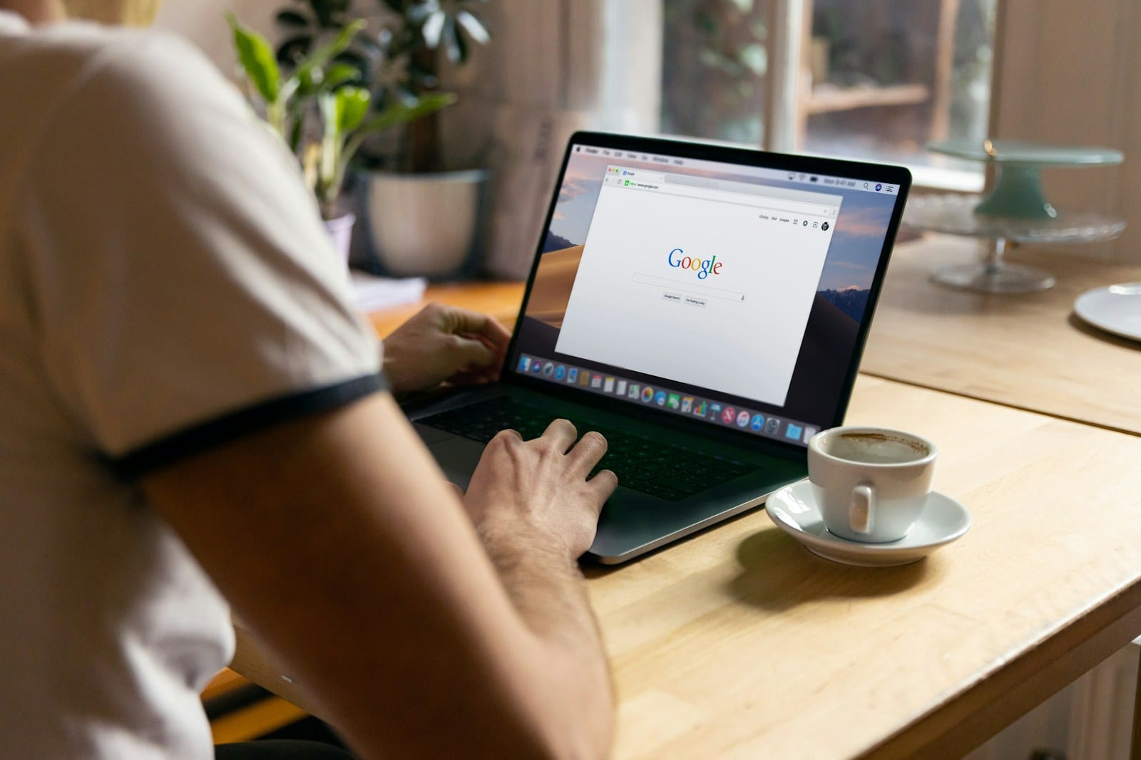 A person searching Google on a MacBook in a cafe.
