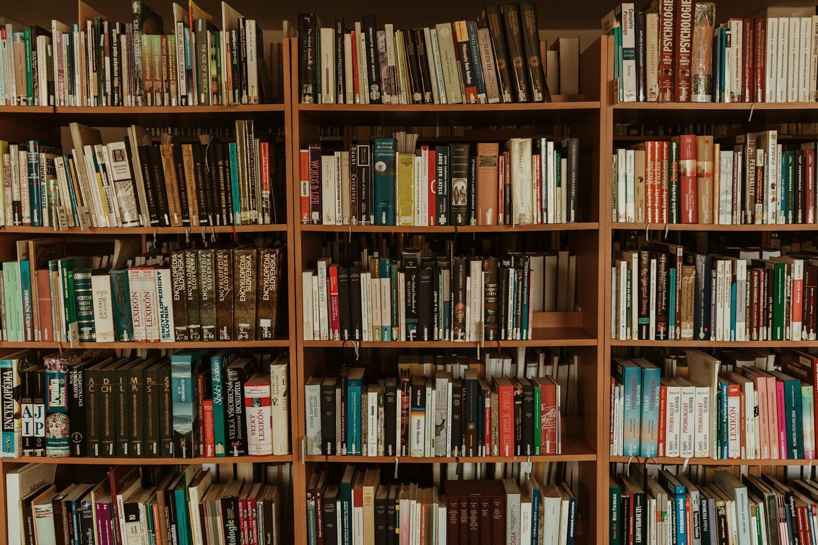 Shelves of reference volumes and encyclopedias in a library — the kind of corroborated source layer a language model draws on when it decides what to cite.